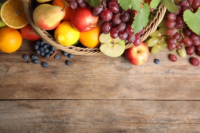 Wicker basket with different fruits and berries on wooden table, flat lay. Space for text