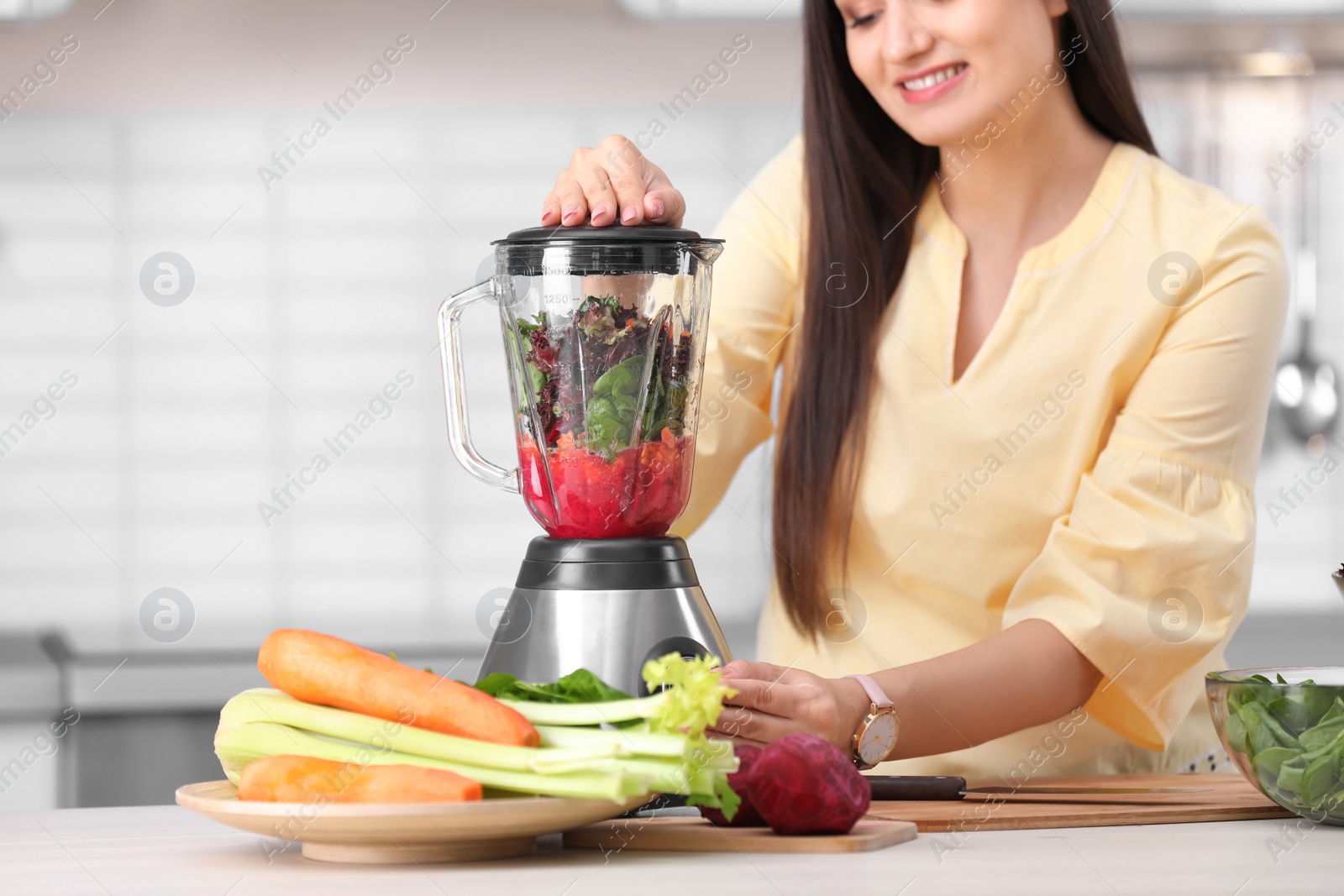 Photo of Young woman preparing tasty healthy smoothie at table in kitchen