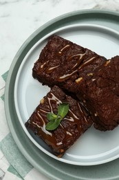 Photo of Delicious chocolate brownies with nuts, caramel sauce and fresh mint on white marble table, top view