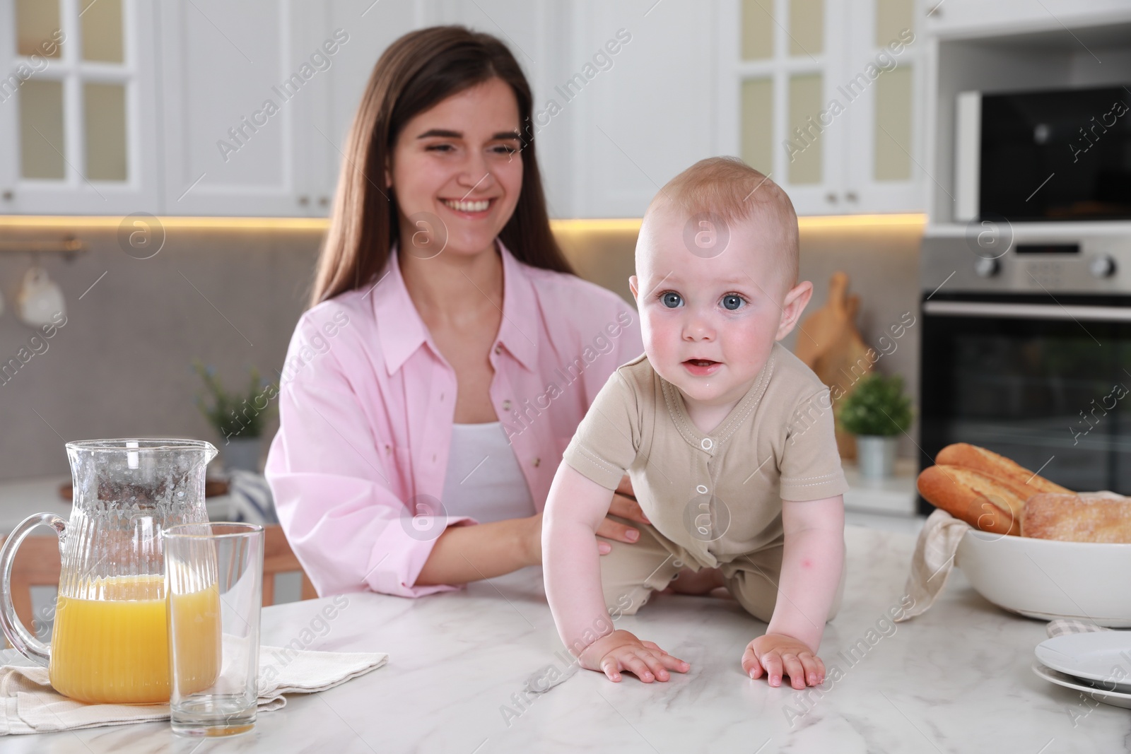 Photo of Happy young woman and her cute little baby spending time together in kitchen