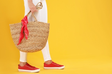 Young woman with stylish straw bag on yellow background, closeup. Space for text