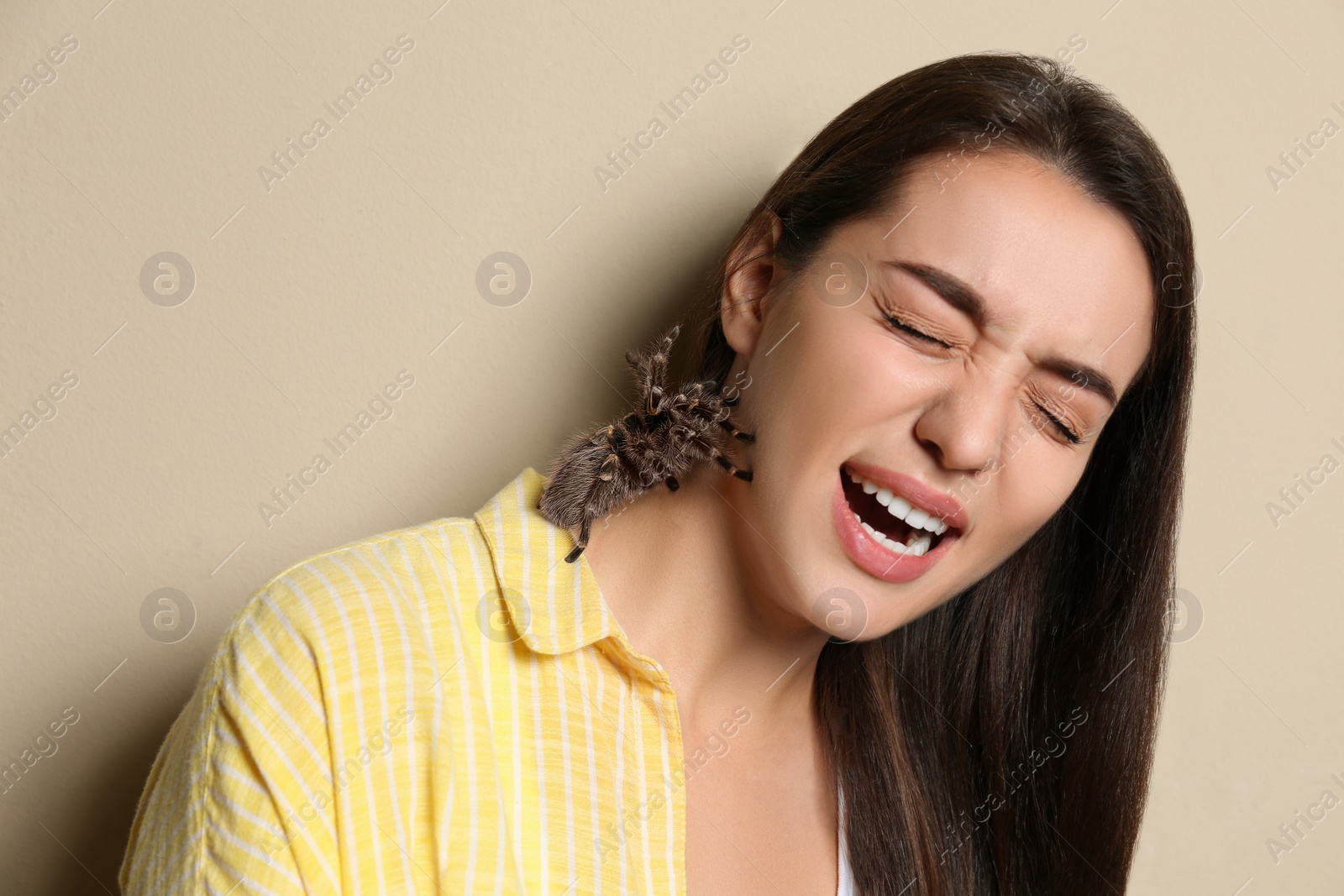 Photo of Scared young woman with tarantula on beige background. Arachnophobia (fear of spiders)