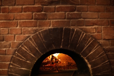 Photo of Brick oven with burning firewood and pizzas indoors