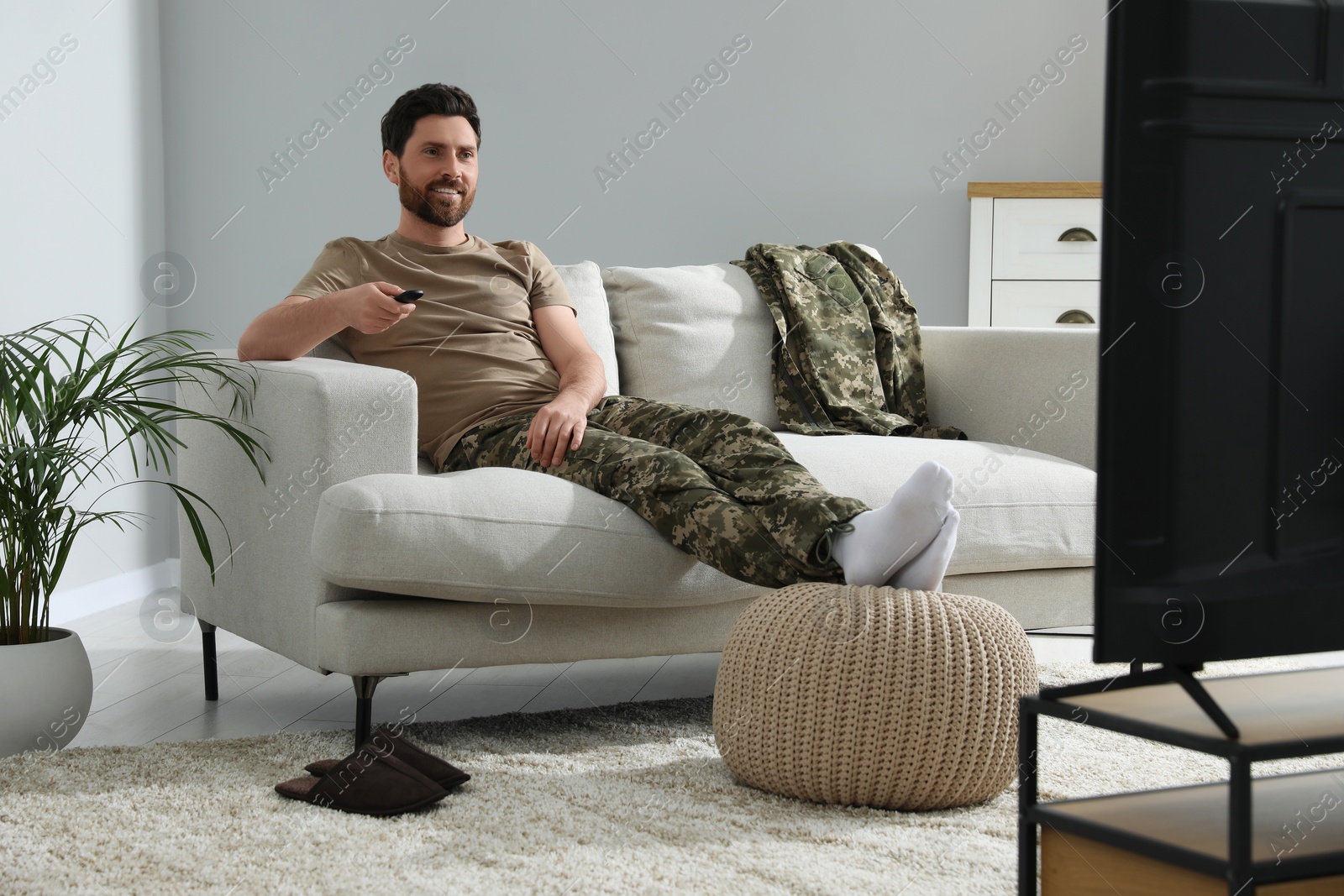 Photo of Happy soldier watching TV on sofa in living room. Military service