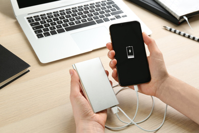 Photo of Woman charging mobile phone with power bank at wooden table, closeup