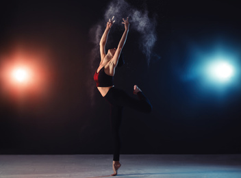 Professional acrobat with chalk powder exercising in dark studio