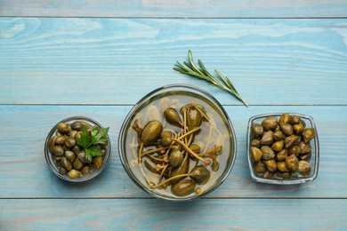 Photo of Tasty capers, rosemary and parsley on light blue wooden table, flat lay