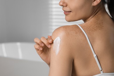 Young woman applying body cream onto shoulder in bathroom, closeup. Space for text