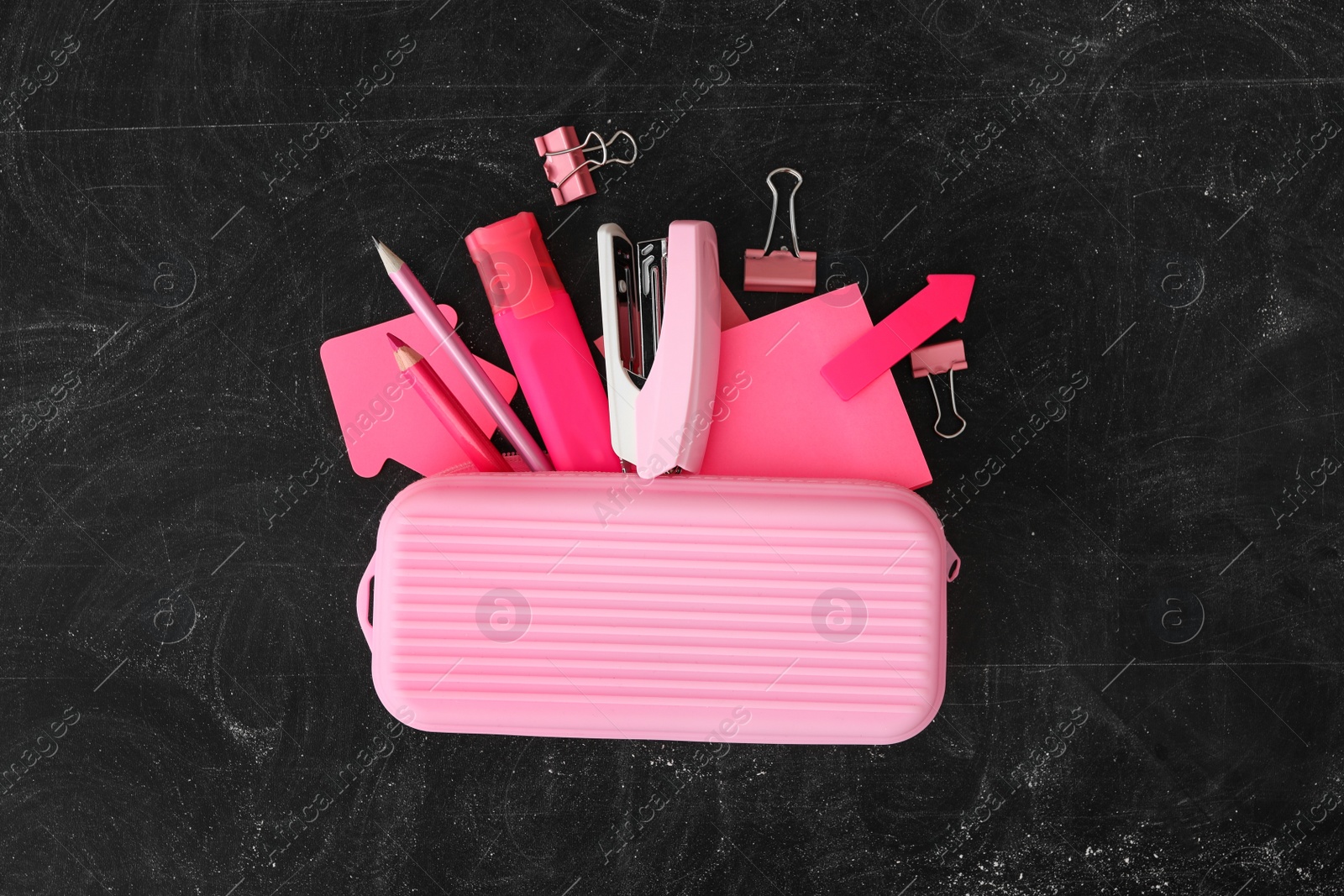 Photo of Pink pencil case and different stationery on blackboard, flat lay. Back to school