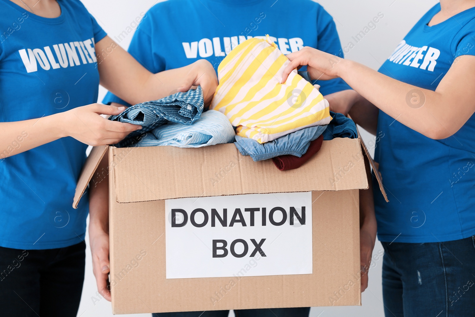 Photo of Volunteers putting clothes in donation box on light background