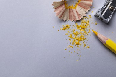 Photo of Yellow pencil, shaving, crumbs and sharpener on grey background, flat lay. Space for text