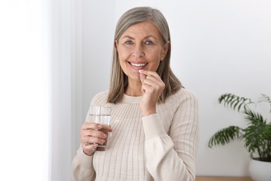 Beautiful woman taking vitamin pill at home