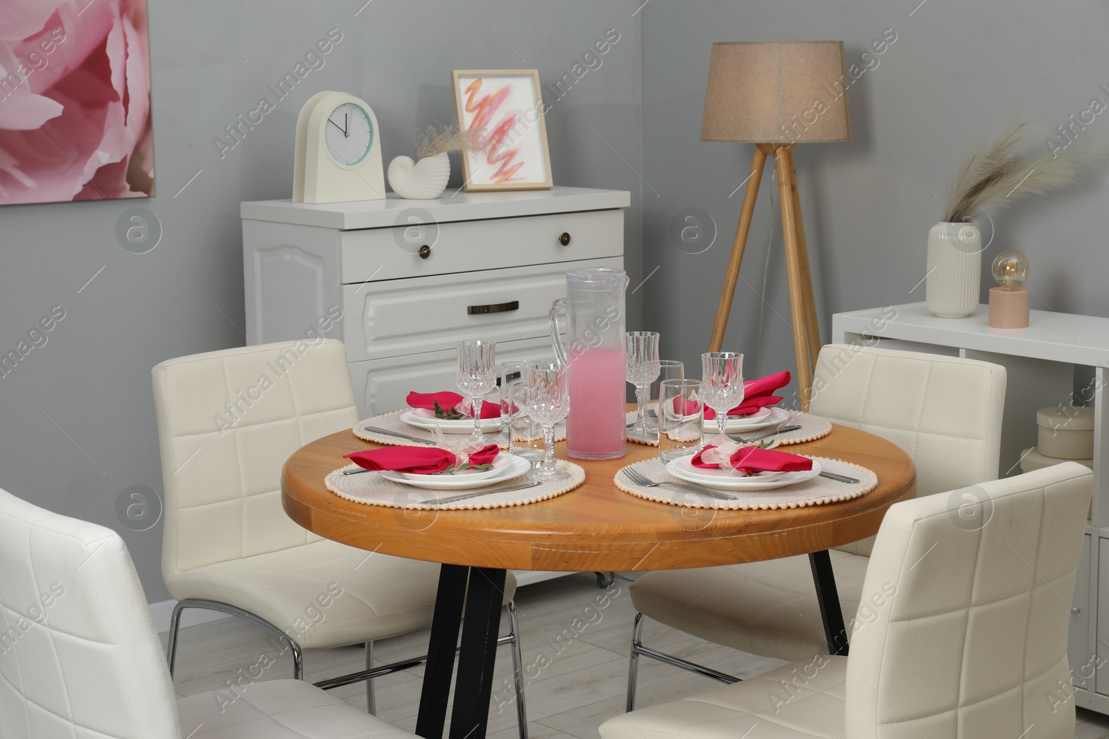 Photo of Color accent table setting. Glasses, plates, jug of beverage and pink napkins in dining room