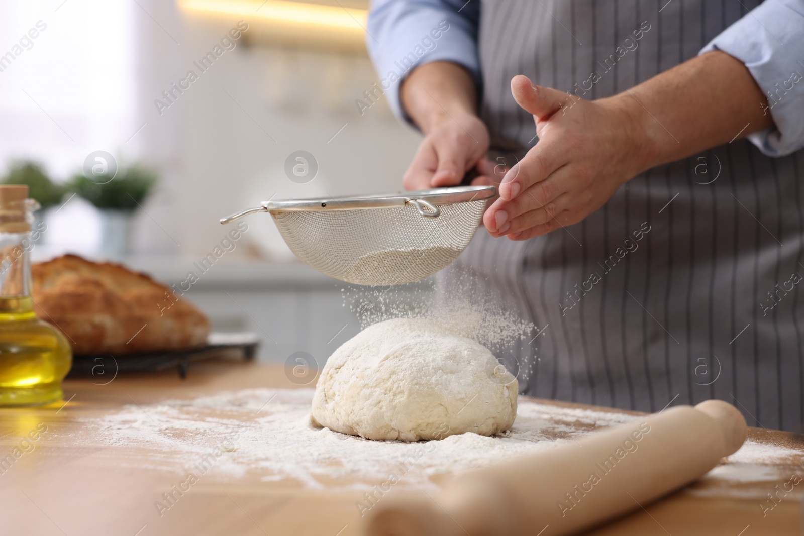 Photo of Making bread. Man sprinkling flour onto dough at wooden table in kitchen, closeup