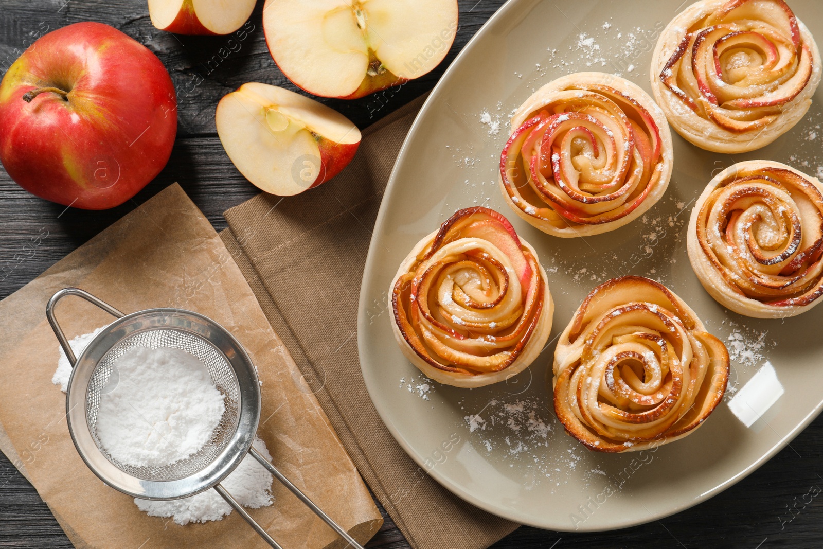 Photo of Freshly baked apple roses on dark wooden table, flat lay. Beautiful dessert