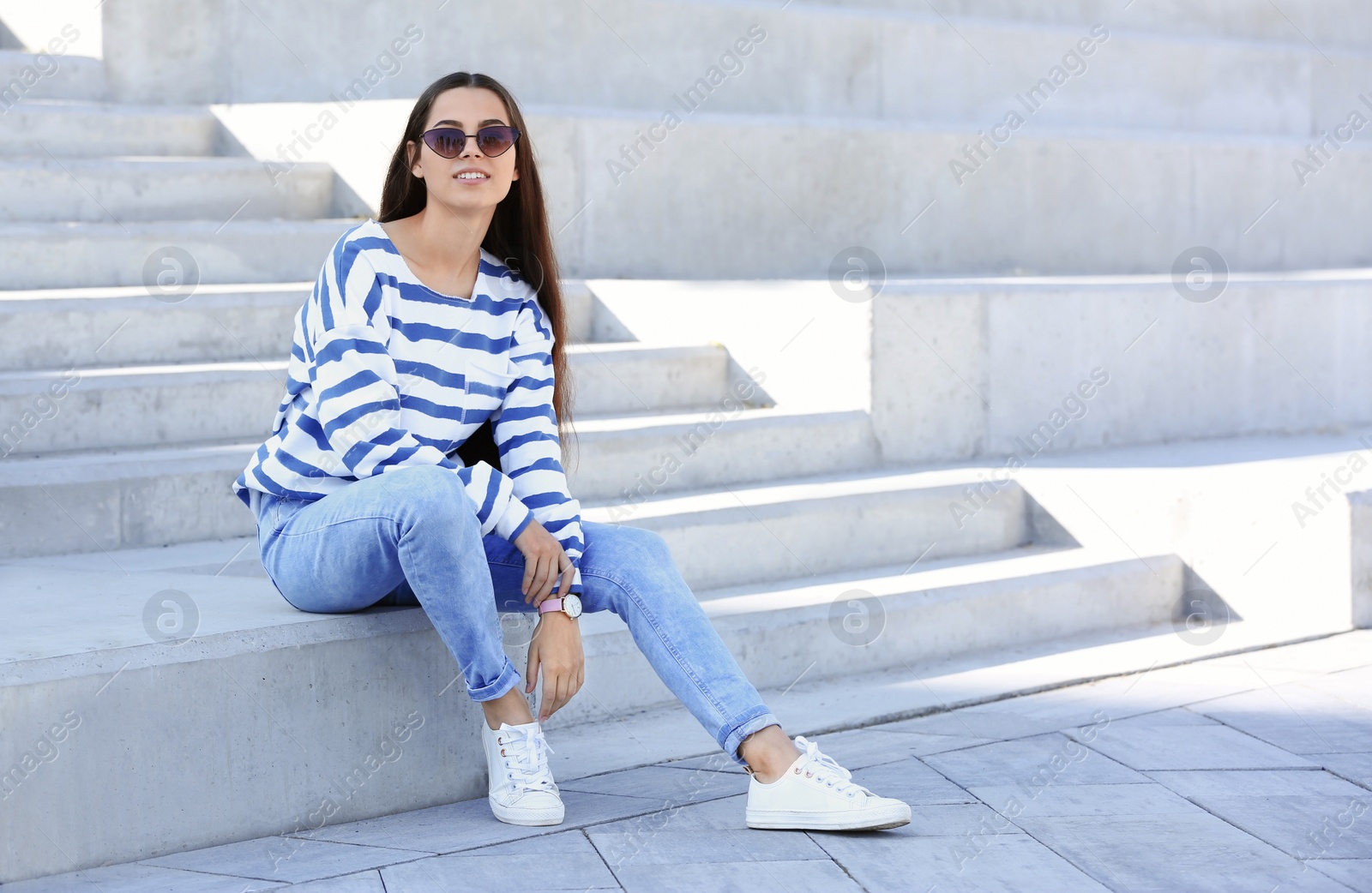 Photo of Young hipster woman in stylish jeans sitting on stairs outdoors