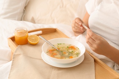 Sick woman with thermometer and bowl of fresh homemade soup to cure flu on tray in bed, closeup