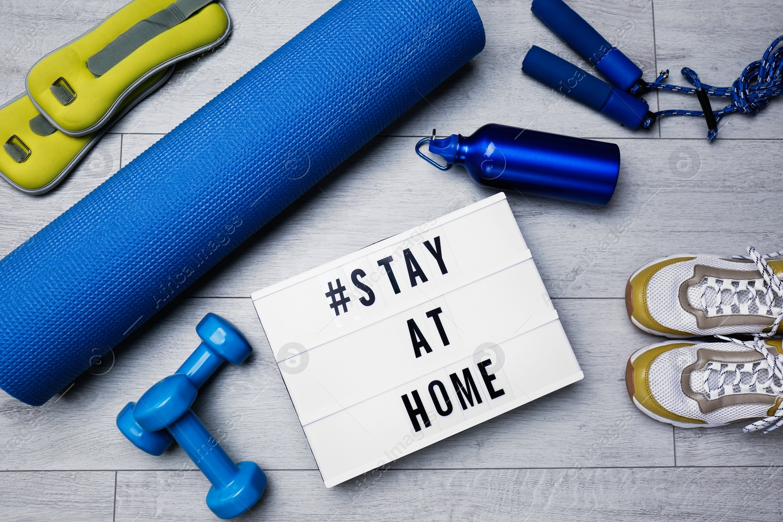 Photo of Sport equipment and lightbox with hashtag STAY AT HOME on floor, flat lay. Message to promote self-isolation during COVID‑19 pandemic