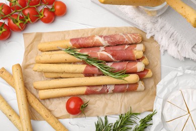 Photo of Delicious grissini sticks with prosciutto and snacks on white table, flat lay