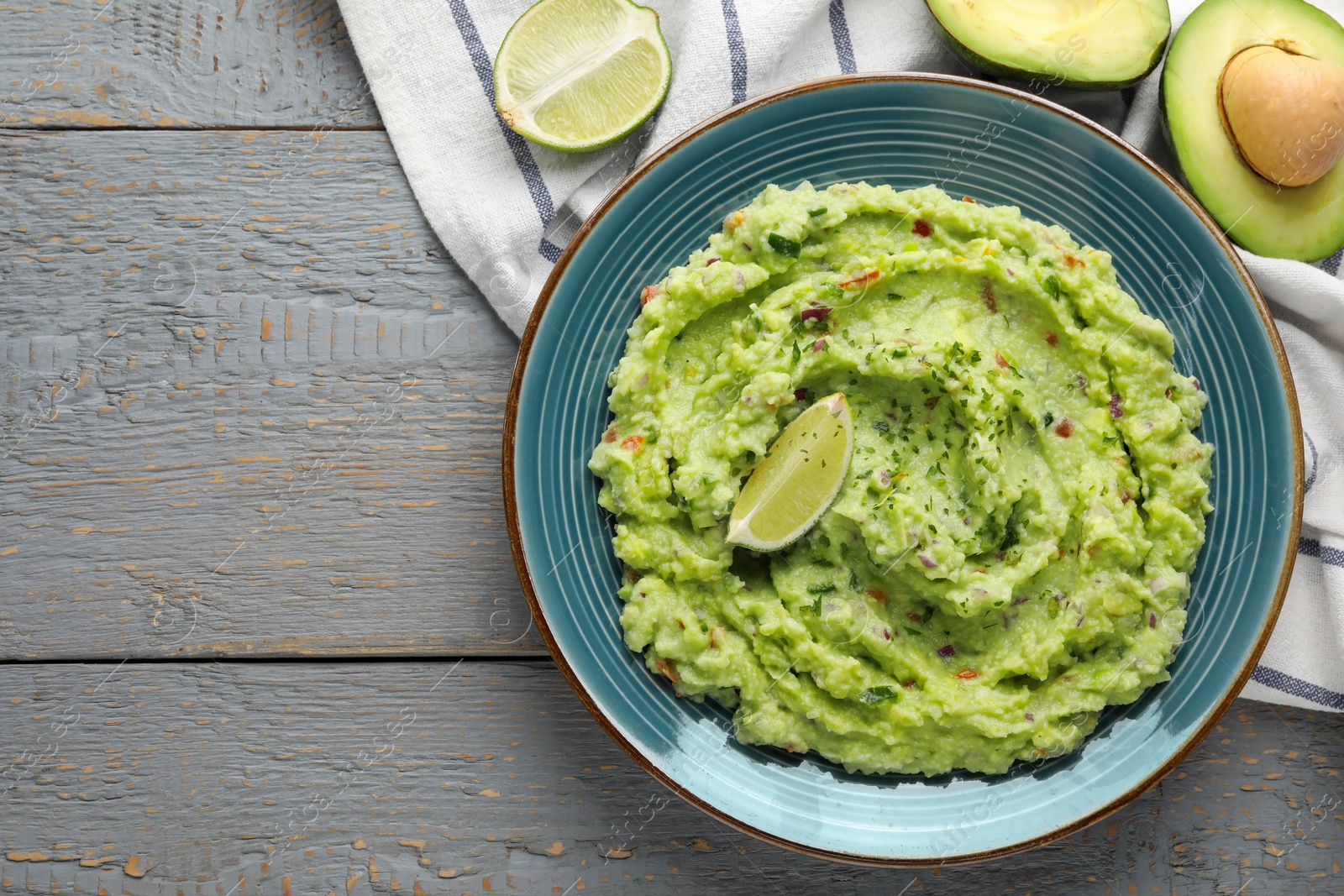 Photo of Delicious guacamole with lime and fresh avocado on grey wooden table, flat lay. Space for text