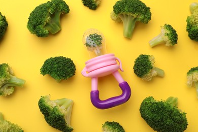 Photo of Nibbler with boiled broccoli on yellow background, flat lay. Baby feeder
