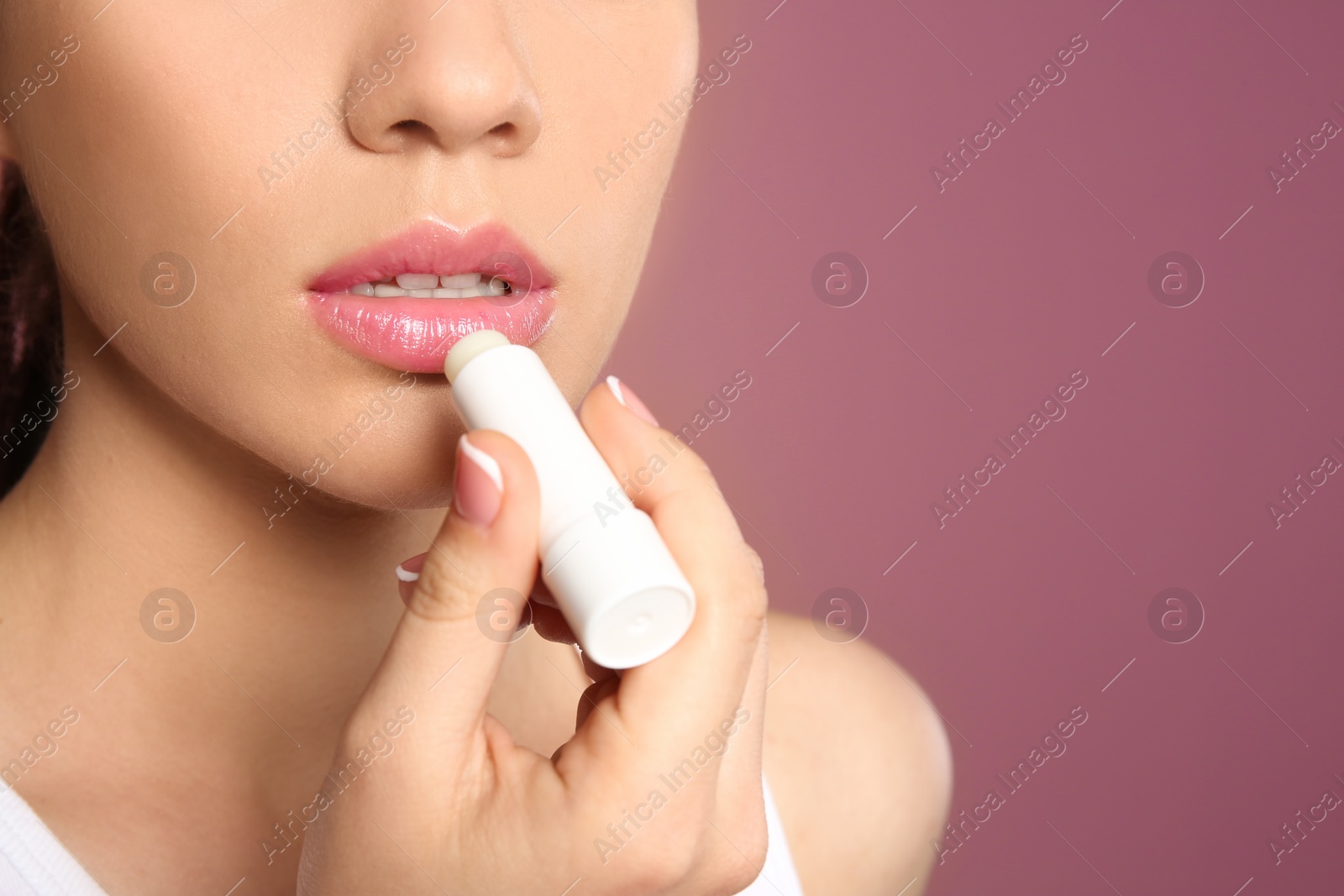 Photo of Young woman applying balm on her lips against color background, closeup