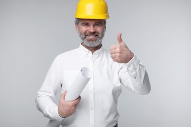 Photo of Architect in hard hat holding draft and showing thumb up on grey background