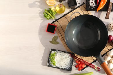 Photo of Wok, chopsticks and different products on white wooden table, flat lay. Space for text