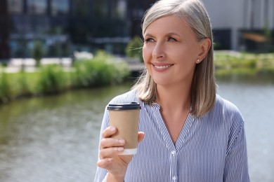 Photo of Portrait of happy senior woman with paper cup of coffee outdoors, space for text