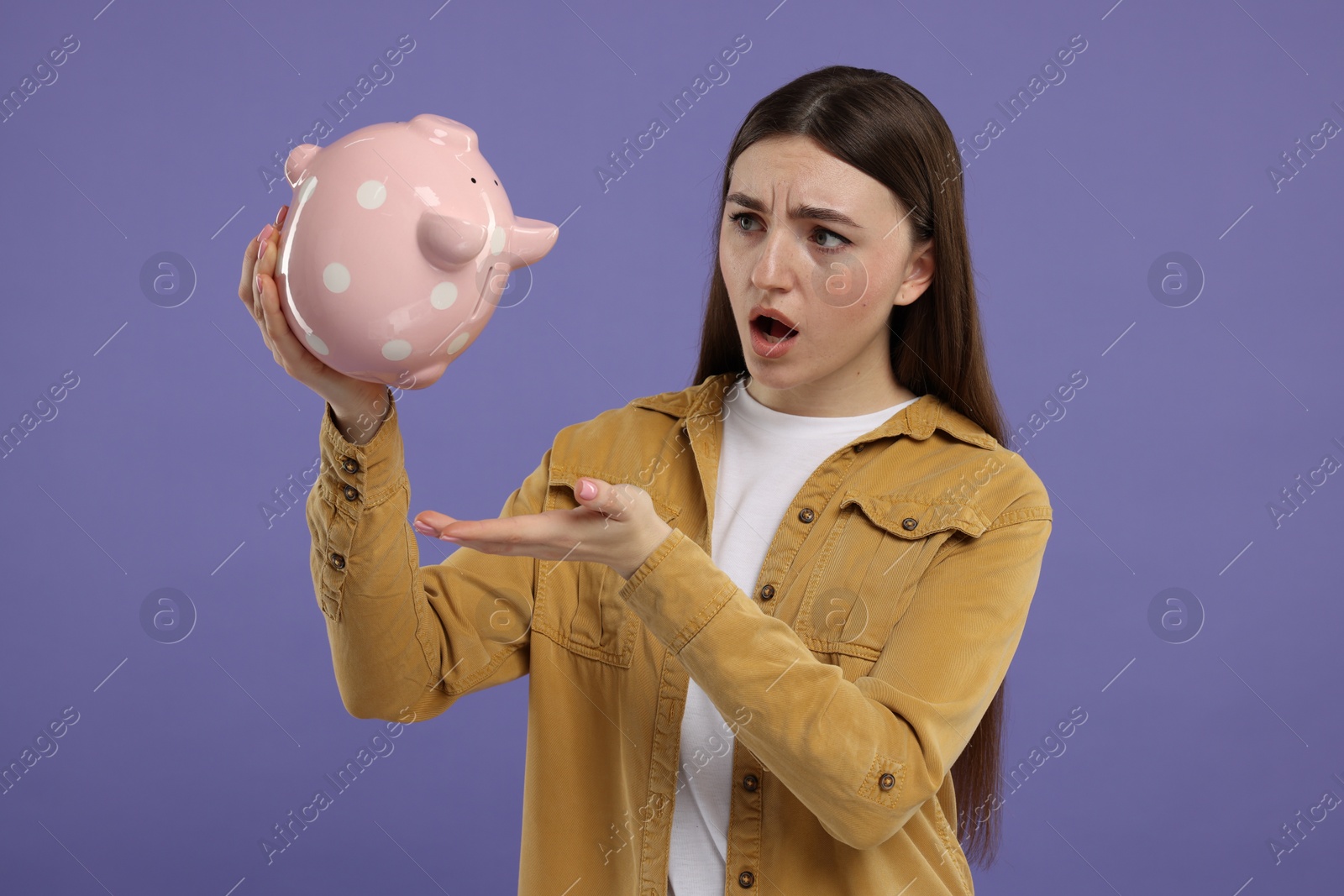 Photo of Sad woman with piggy bank on purple background