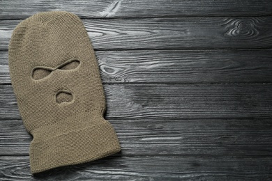 Beige knitted balaclava on black wooden table, top view. Space for text