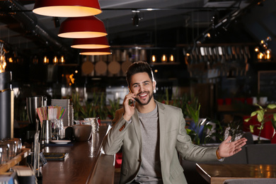 Photo of Young business owner talking on phone in his cafe