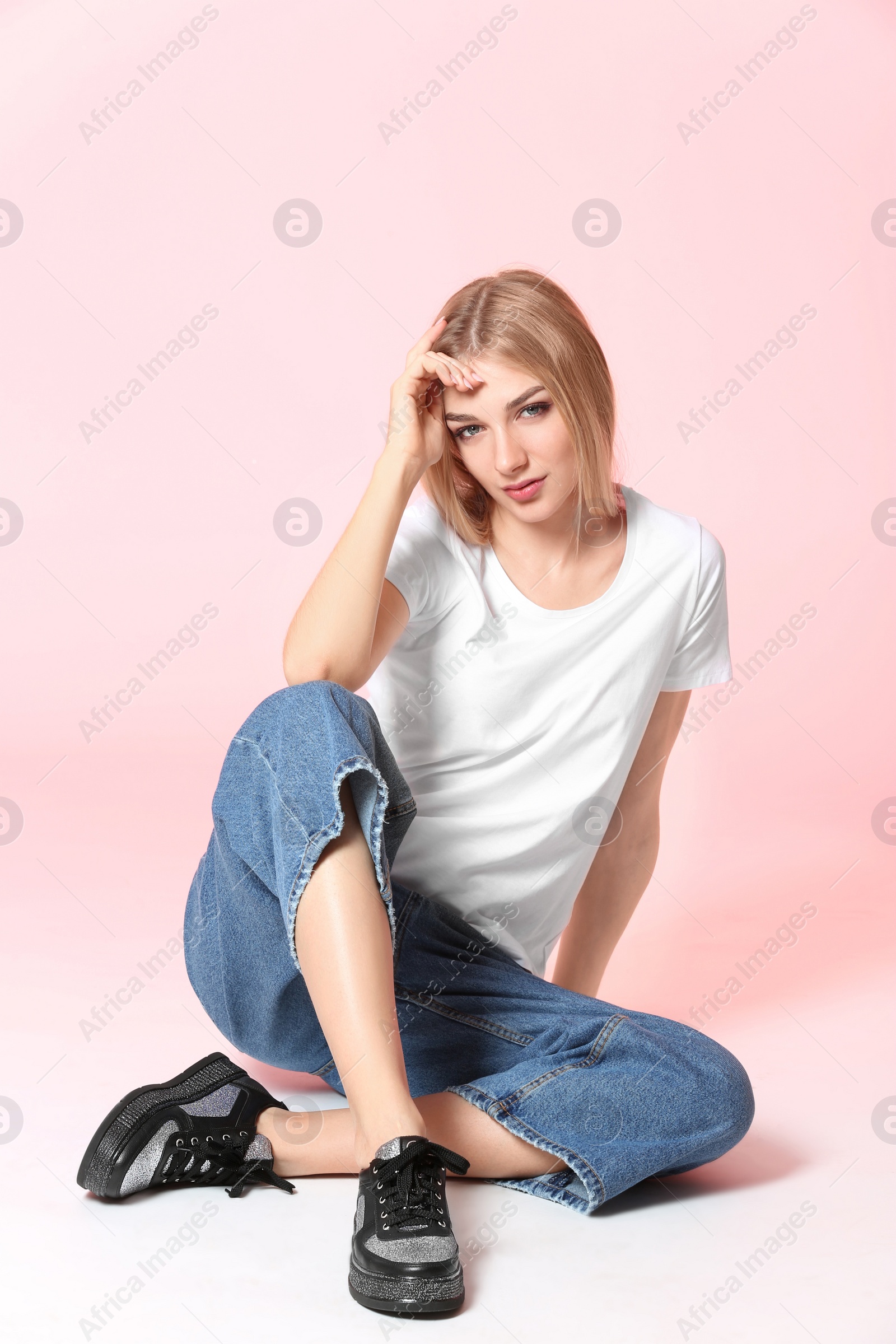 Photo of Fashionable young woman in stylish shoes sitting on color background