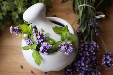 Photo of Mortar with fresh lavender flowers, mint and pestle on wooden table, closeup