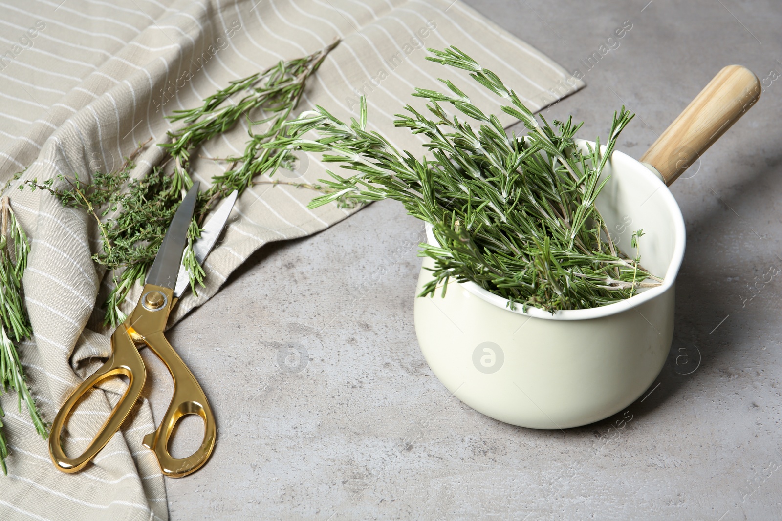 Photo of Fresh green rosemary in cookware and scissors on table. Aromatic herbs