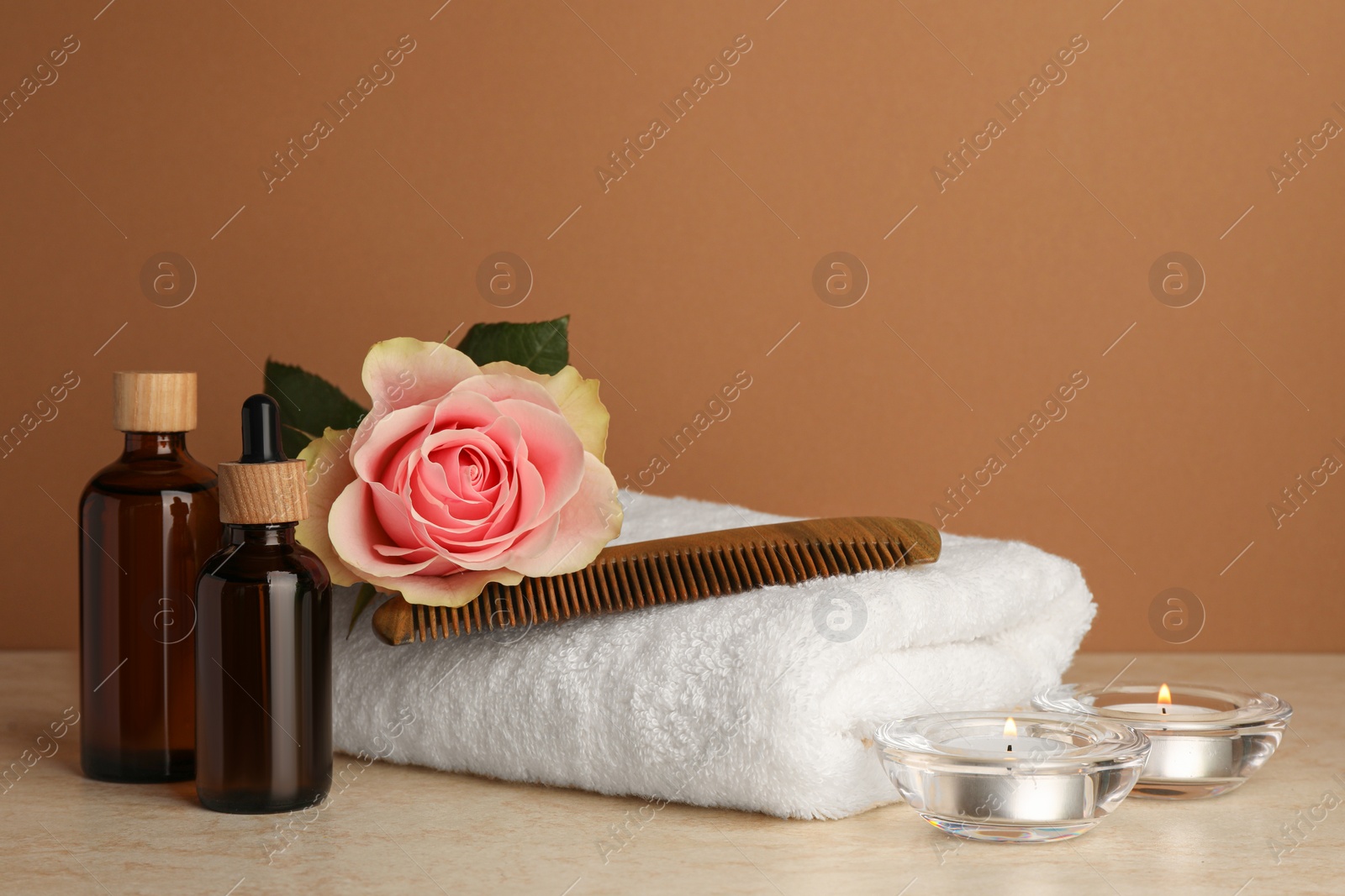 Photo of Composition with different spa products, beautiful flower and burning candles on beige table against brown background. Space for text