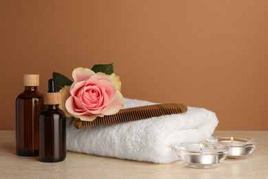 Photo of Composition with different spa products, beautiful flower and burning candles on beige table against brown background. Space for text