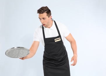 Photo of Clumsy waiter dropping empty tray on light background