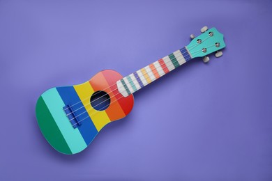 Photo of Colorful ukulele on purple background, top view. String musical instrument