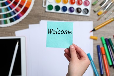 Image of Woman holding paper note with word Welcome over her office desk, top view