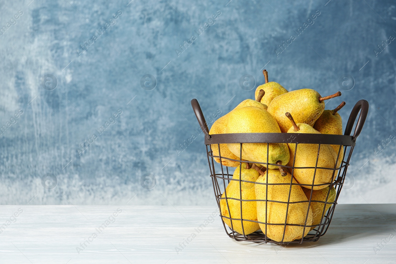 Photo of Basket of fresh ripe pears on table against color background with space for text