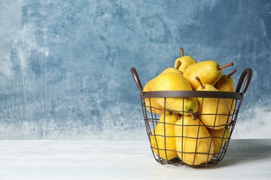 Basket of fresh ripe pears on table against color background with space for text