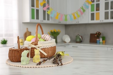 Photo of Wicker baskets with Easter eggs and willow twigs at white marble table in kitchen, space for text