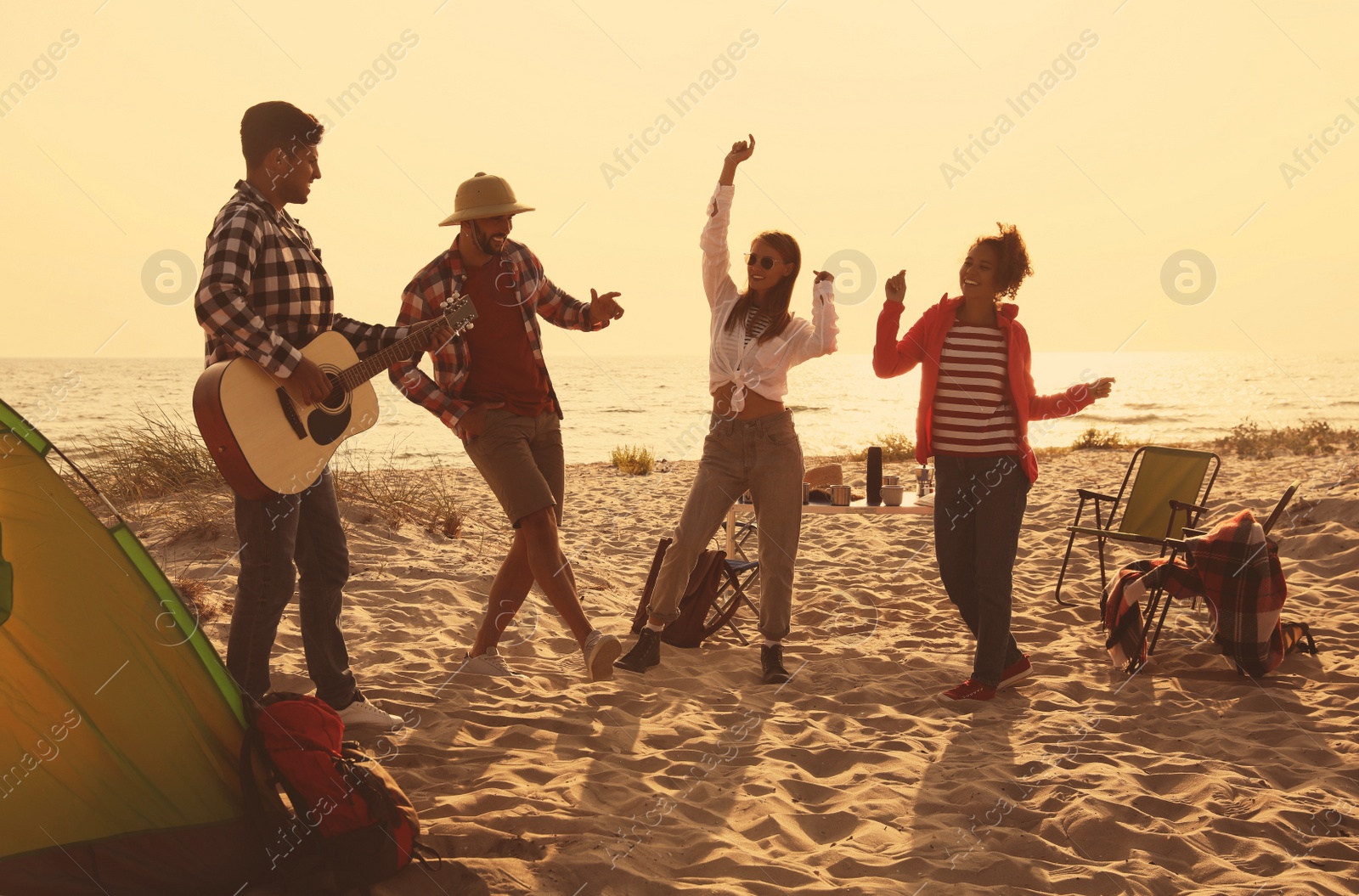 Image of Friends having party near camping tent on sandy beach