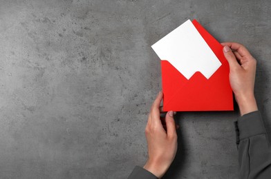 Woman holding letter envelope with card at grey textured table, top view. Space for text