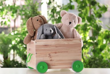 Photo of Wooden cart with stuffed toys on table against blurred background