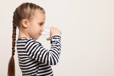 Photo of Cute little girl drinking fresh water from glass on white background. Space for text
