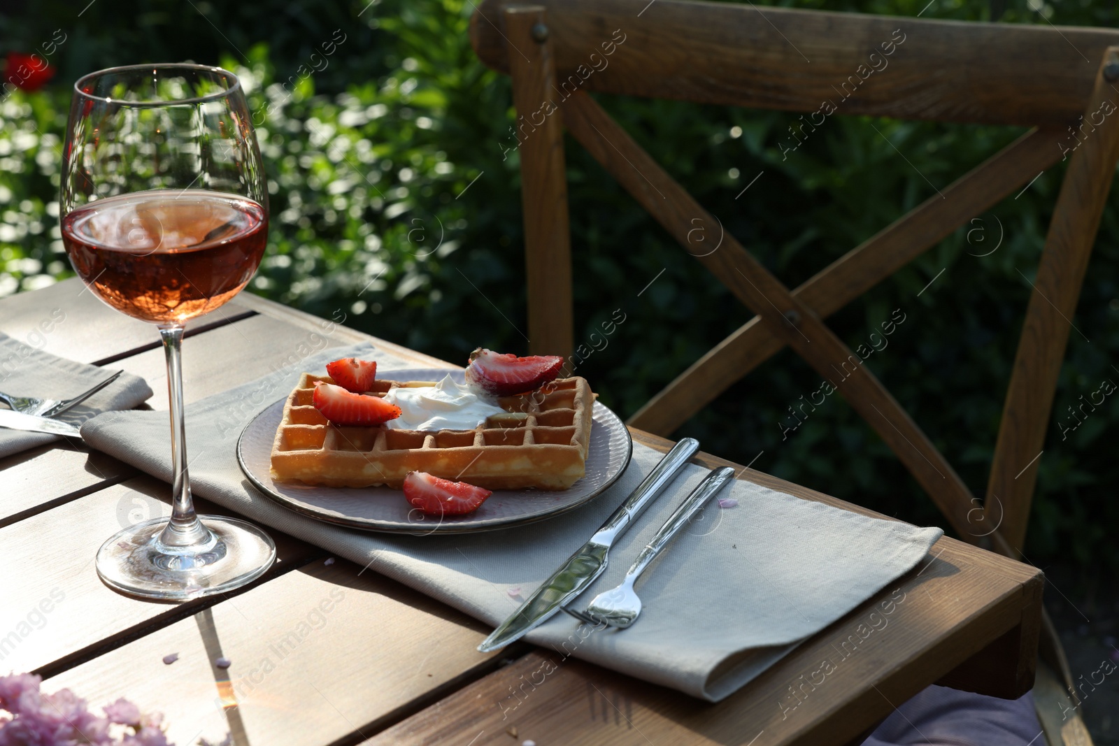 Photo of Delicious Belgian waffle with fresh strawberries and wine served on table in spring garden