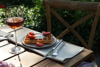 Photo of Delicious Belgian waffle with fresh strawberries and wine served on table in spring garden