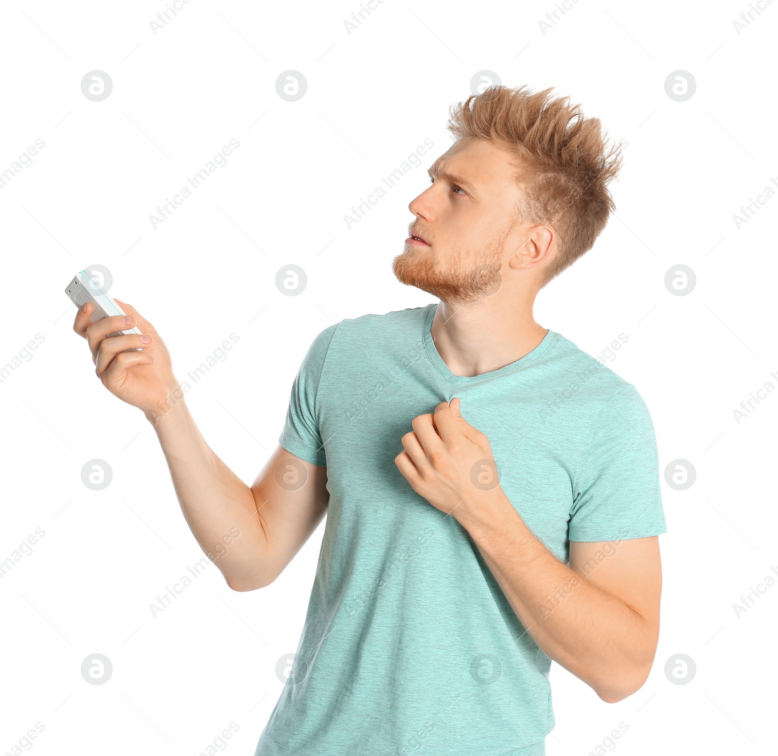 Photo of Young man with air conditioner remote suffering from heat on white background